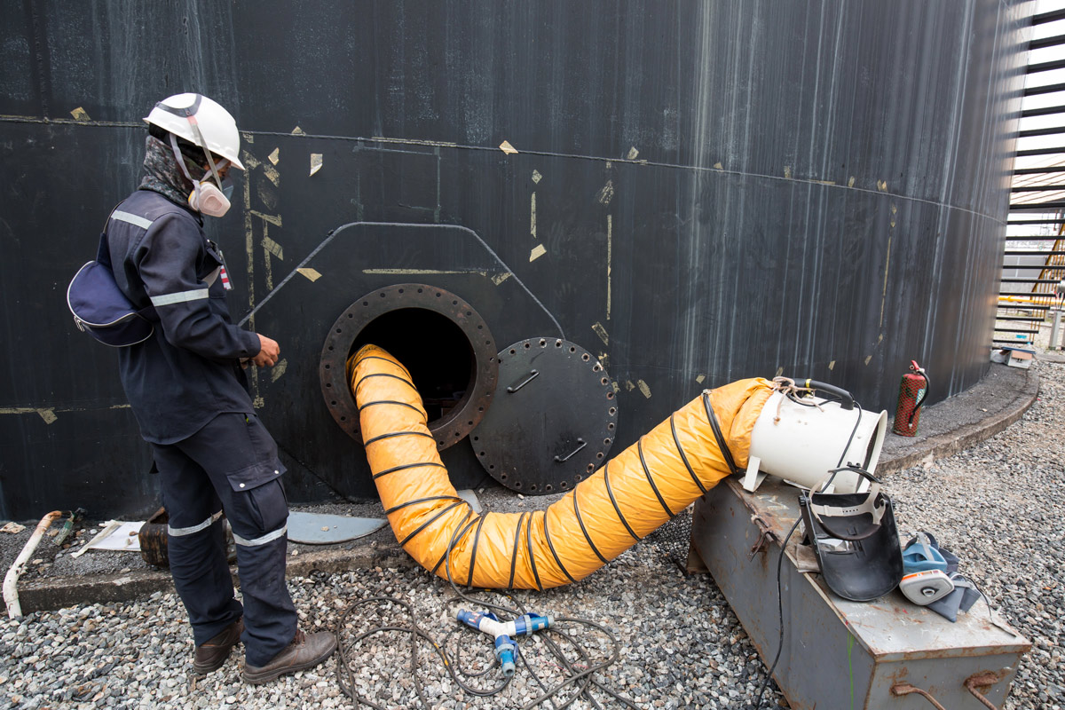 Man in HAZMAT gear at an oil tank, protected from hydrogen sulfide